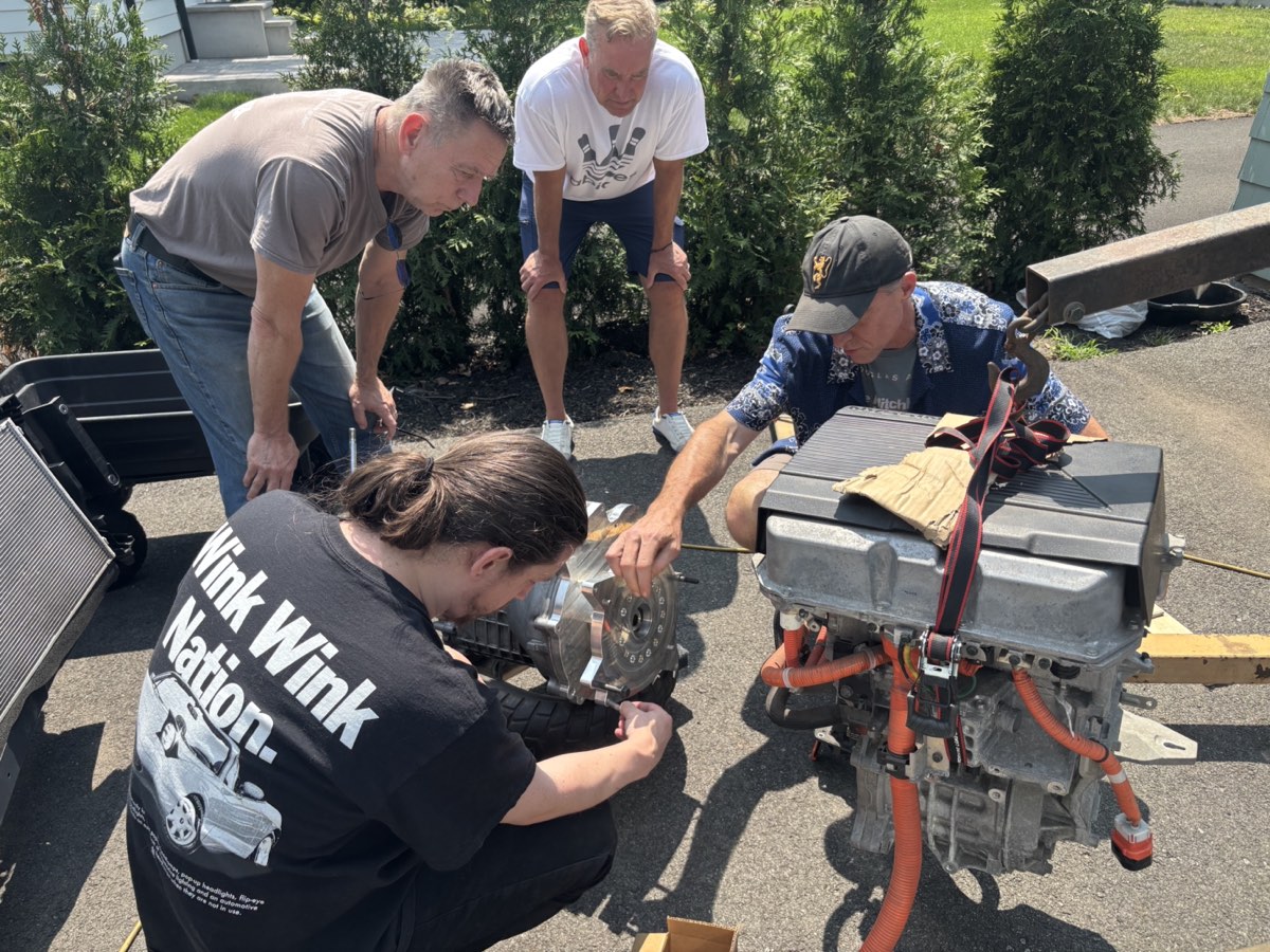 Four builders crouched over a Nissan Leaf motor and adapter plate in a driveway.